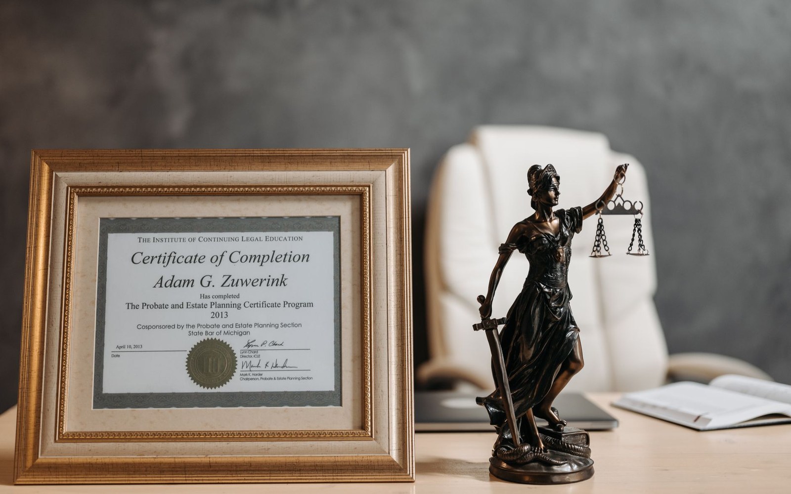 Framed legal certificate beside a bronze Lady Justice statue on an office desk