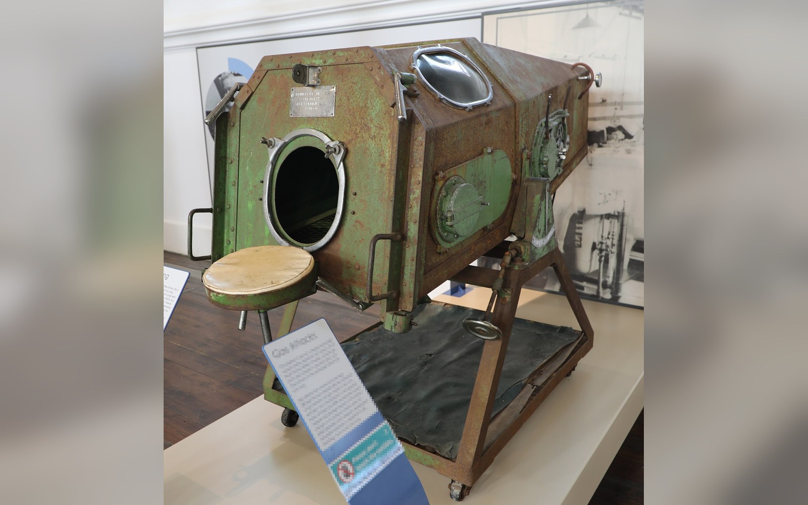 A rusted metal iron lung with round portholes displayed on a museum stand