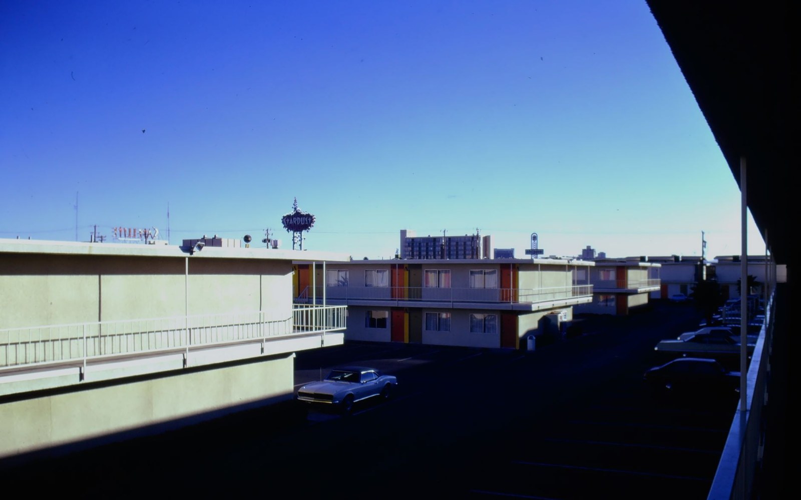 Vintage motel courtyard with striped balcony trim, parked cars, and distant Stardust sign