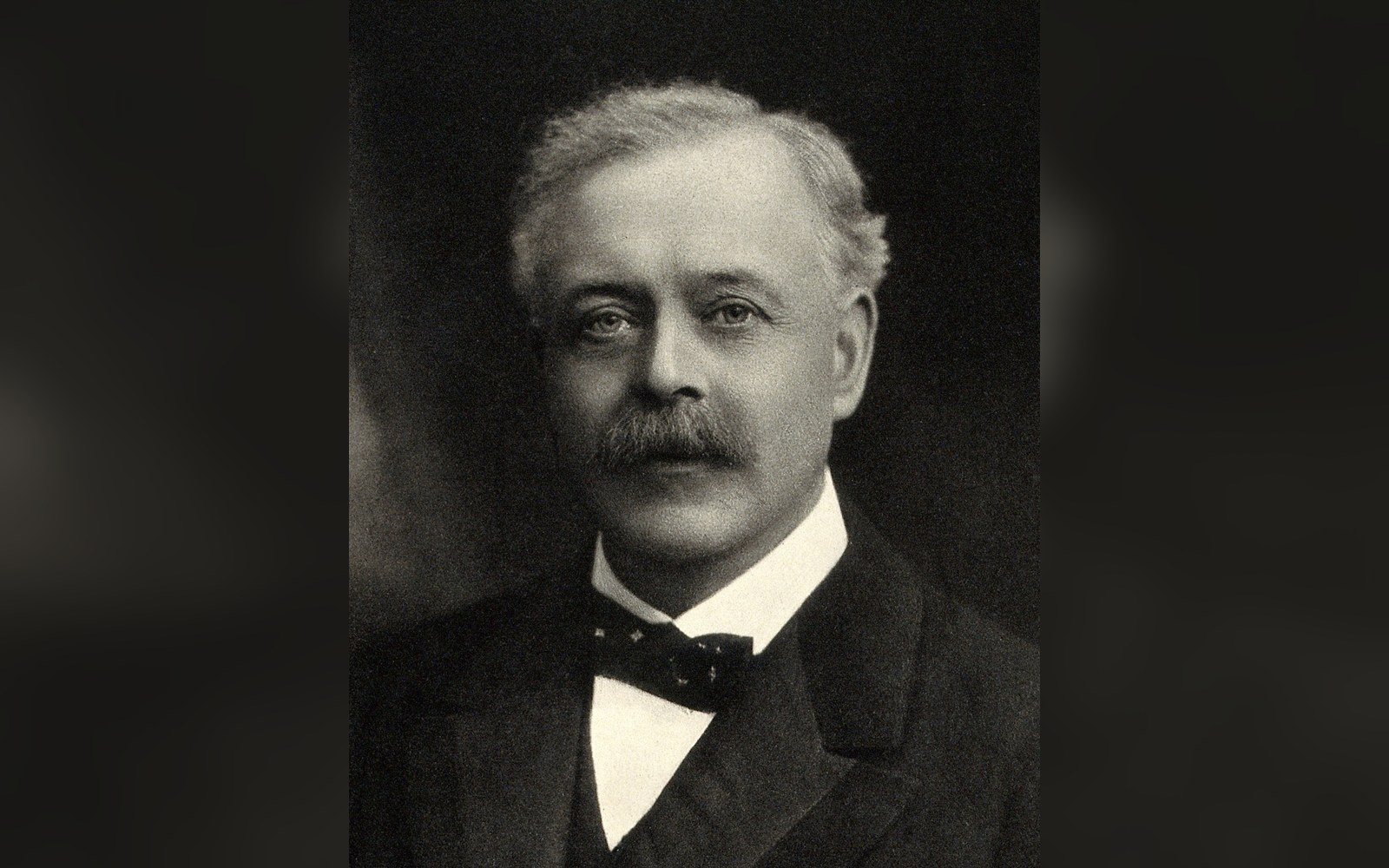Black and white portrait of a mustached man in a suit with a bow tie