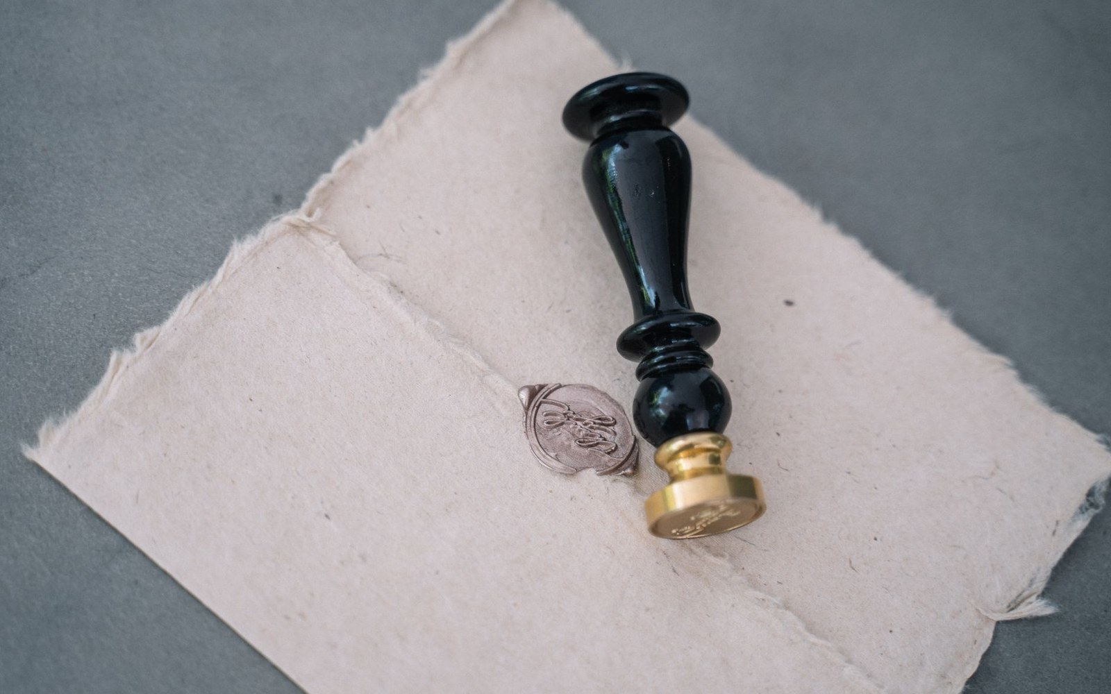 A brass wax seal stamp resting beside an impressed wax seal on textured paper