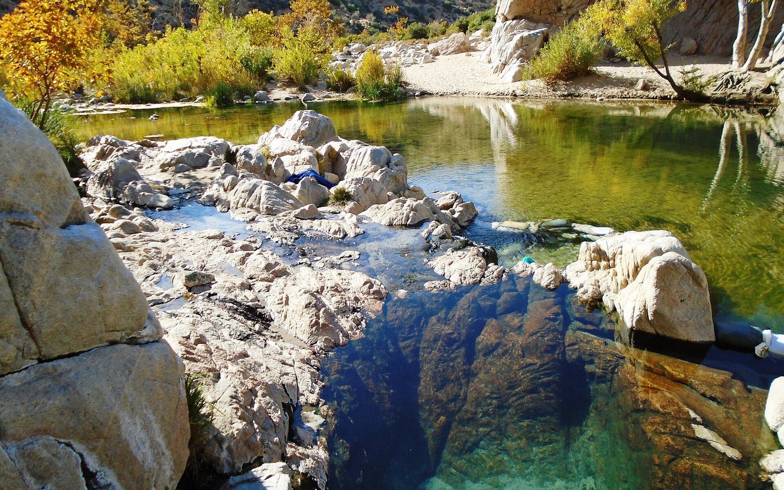 Rock-rimmed natural pool at Deep Creek Hot Springs surrounded by autumn foliage and boulders