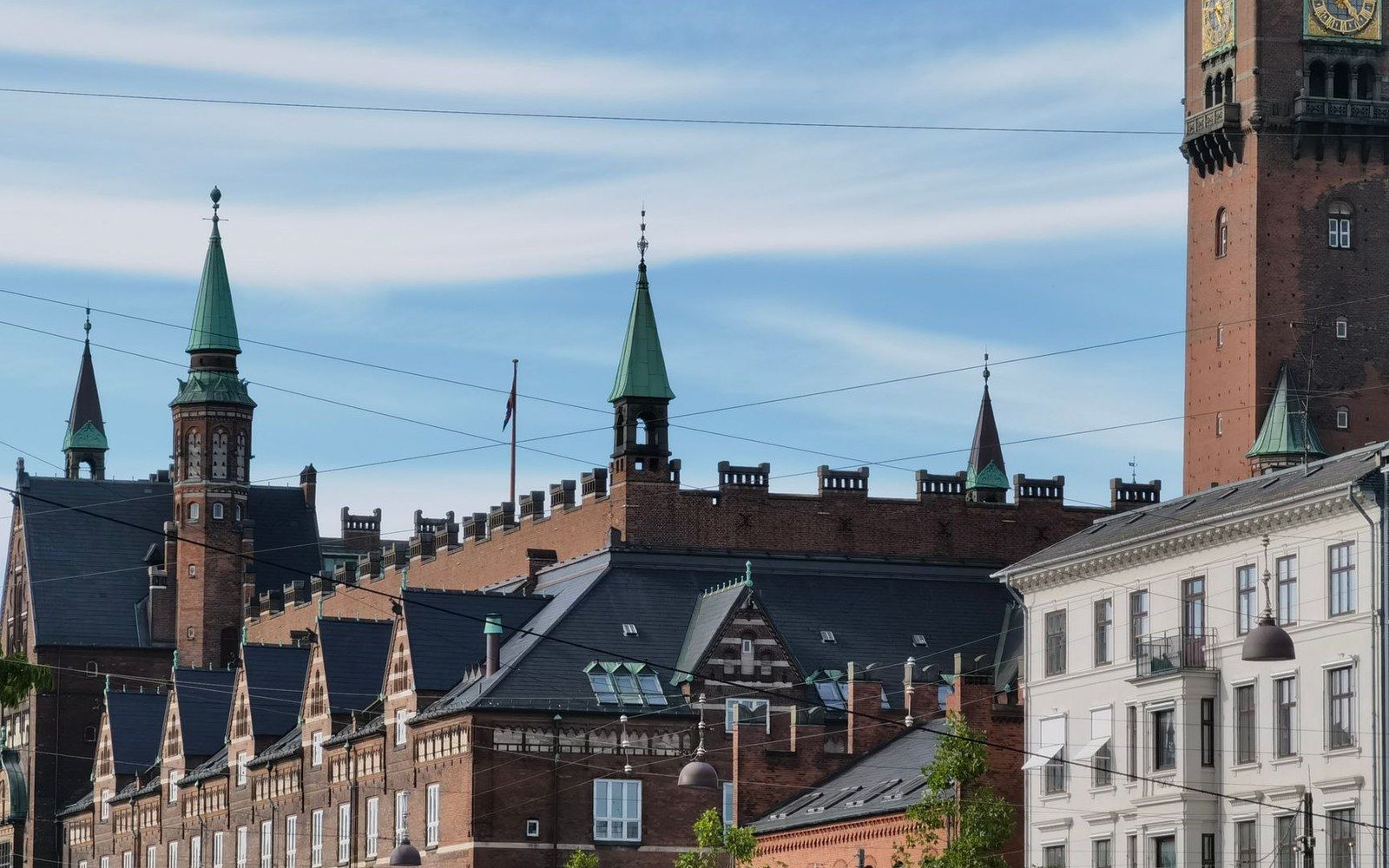Copper-spired towers rise above a red-brick building with a stepped, castellated roofline