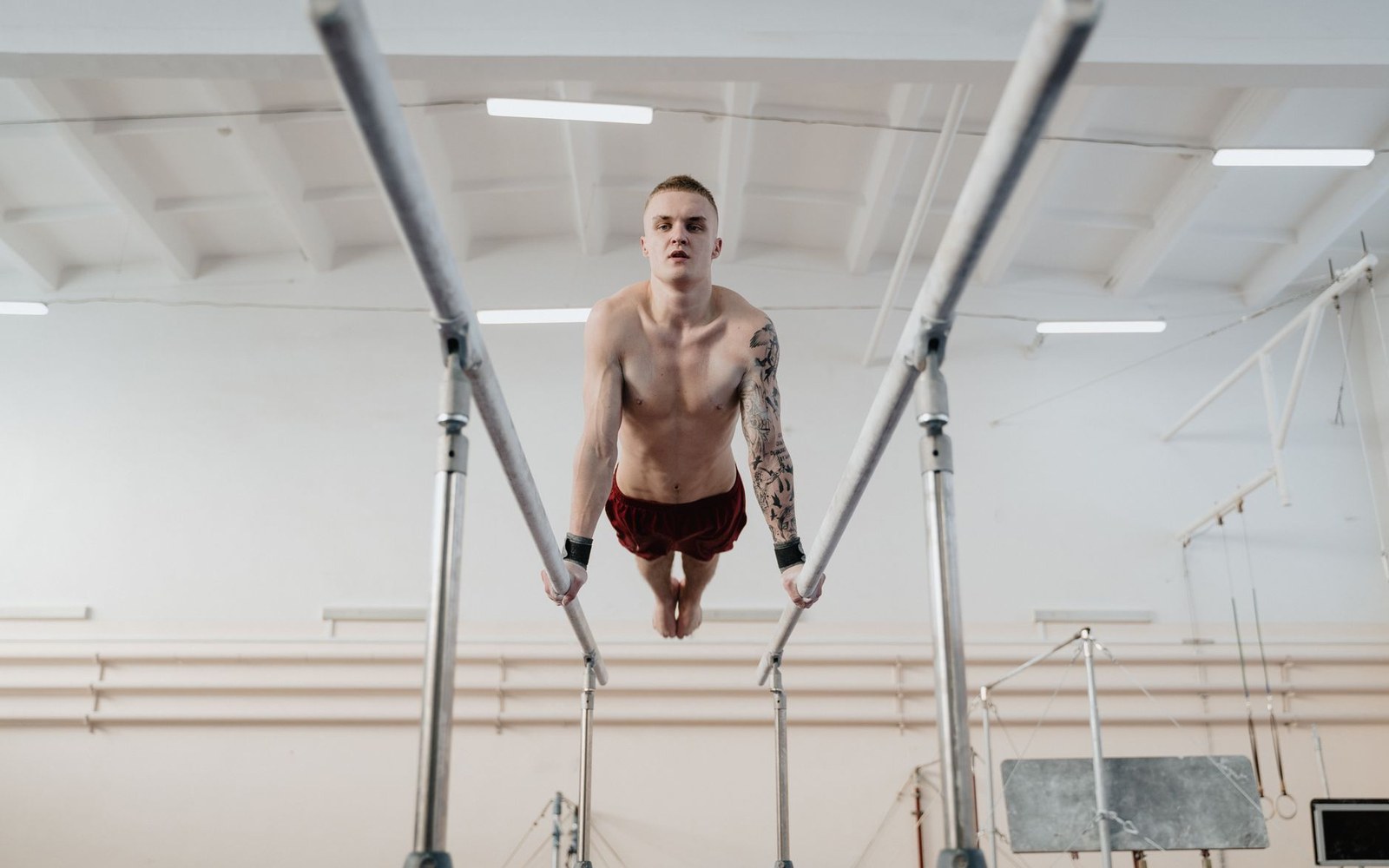 Interior of a 1930s hospital gymnasium: parallel bars in the foreground, wall-mounted apparatus behind, an adult figure present at scale — landscape